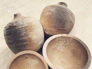 Två runda beige kermaikvaser ligger ned på ett bord. Två runda beige keramikskålar ligger jämte vaserna.