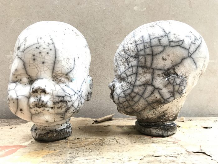 två stycken keramikhuvuden med rakubränning. De är vita med brunt insalg