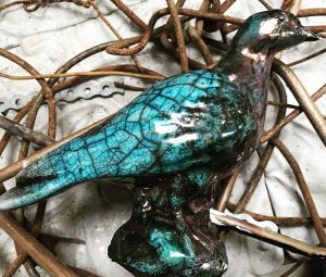 en liggande, turkos keramikfågel med rakumönster.