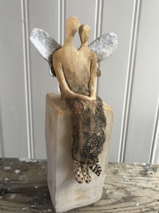 en sittande skulptur i form av två änglar som sitter jämte varandra med änglavingar på ryggen.
